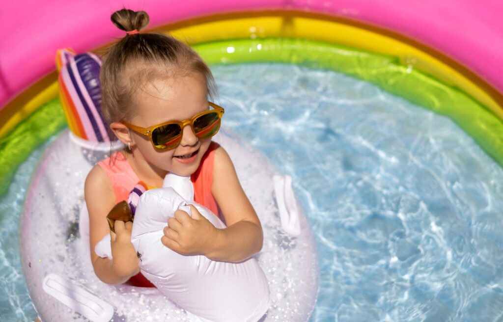 A girl with sunglasses is swimming with a lifebuoy in a inflatable pool
